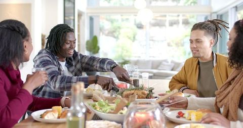 Group of Friends Carving Roasted Chicken and Sharing Plates at Sunlit Home Dinner