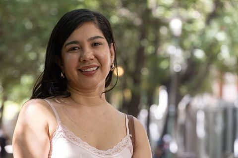 Smiling woman on shaded urban walkway wearing pink camisole and gold hoop earrings