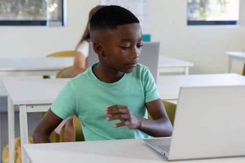 Young black boy using laptop in classroom focusing on schoolwork and technology skills