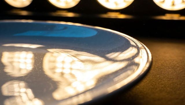 Glossy round plate reflecting warm led lights and dusty rim with soft bokeh