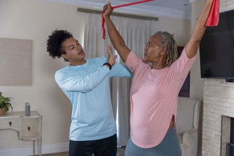 Senior african american woman stretching with red resistance band, trainer guiding at home