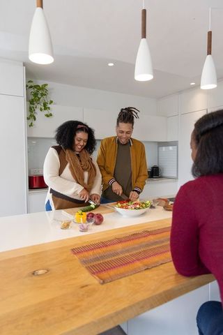 African american couple and friend preparing salad at bright modern kitchen island