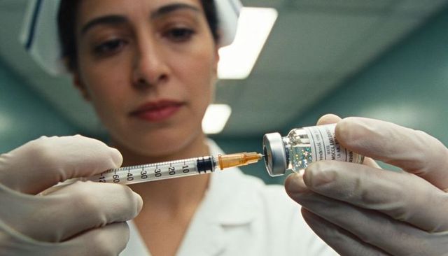 Preparing female nurse drawing vaccine into syringe in sterile clinical environment
