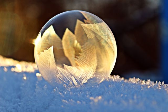 Shows frozen soap bubble with intricate feather-like ice crystals in sunlight. Ideal for winter-themed designs, nature concepts, decorative arts, holiday cards, science and educational materials regarding snow and frost formation.