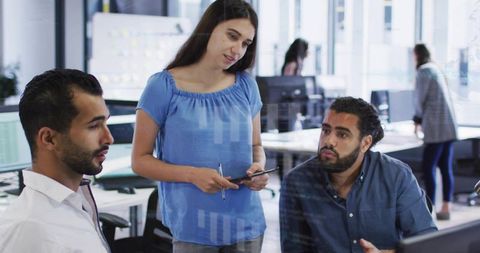 Team collaborating around monitor with standing woman holding tablet in open-plan office