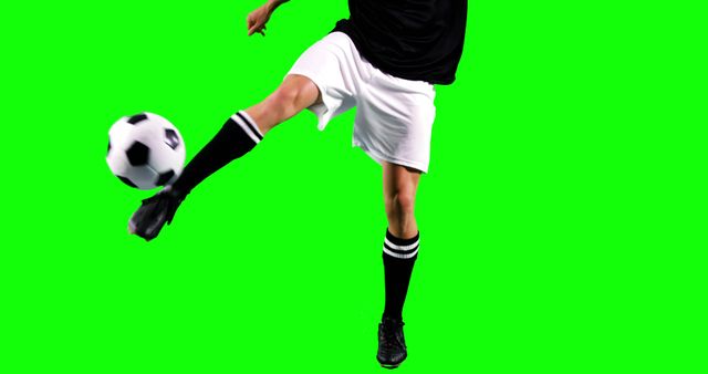 A soccer player is in the midst of kicking a ball during a game or practice session, with copy space. Captured against a green background, the action shot emphasizes the dynamic movement and skill involved in the sport.