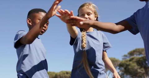 Diverse teens reaching group high-five in sunny park wearing matching light blue t-shirts