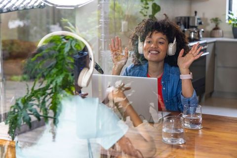 Young professional waving on video call while working from kitchen with headphones