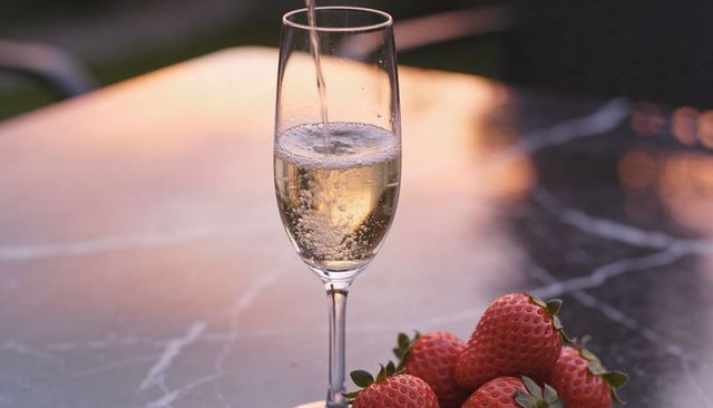 Pouring champagne into flute at dusk with fresh strawberries on marble table