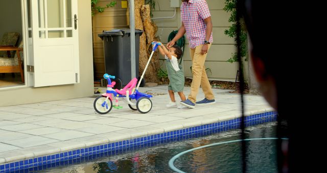Father and son playing with toy tricycle by the poolside - Download Free Stock Images Pikwizard.com