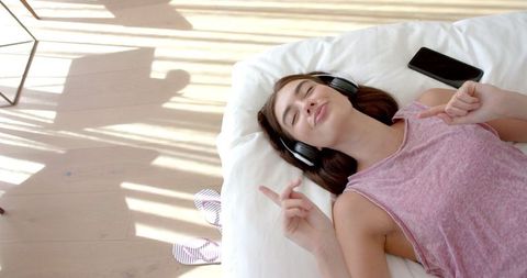 Young Woman Enjoying Music with Headphones on Pillow