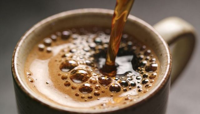 Pouring freshly brewed dark coffee into ceramic mug with rich crema and bubbles