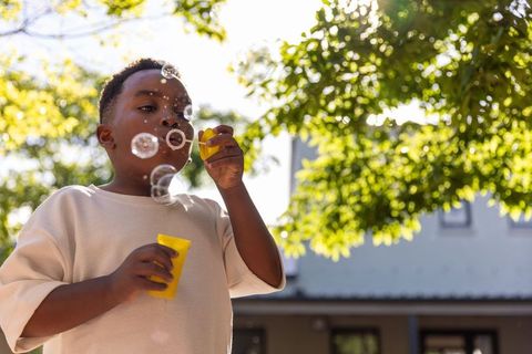 Joyful african american child blowing bubbles in sunlit backyard with yellow wand