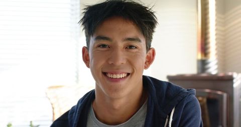 Young man smiling in casual hoodie at home with sunlit window blinds