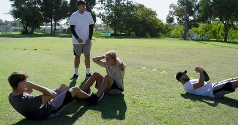 Outdoor group training session with coach leading core strength exercises on grassy field