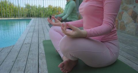 Women meditating poolside on yoga mats in pastel activewear promoting mindfulness