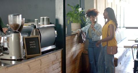 African american friends chatting at rustic coffee counter near espresso machine in cafe