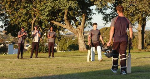 Teen batter walking off to teammates applauding under tree capturing team spirit