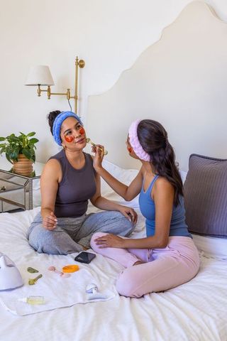 Friends applying facial rollers and hydrogel under-eye patches during relaxing at-home spa