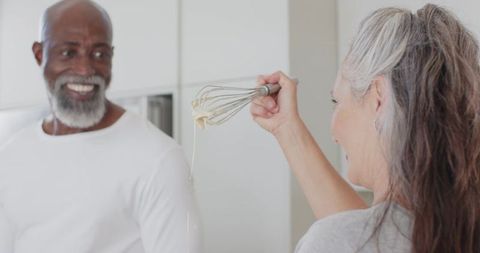 Baking together in modern kitchen smiling senior couple holding whisk with batter
