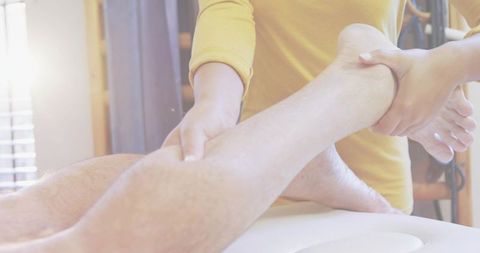 Therapist stretching lower leg and foot during rehabilitation session, backlit