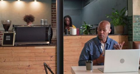 African American man working remotely on laptop in cozy coffeehouse during video call