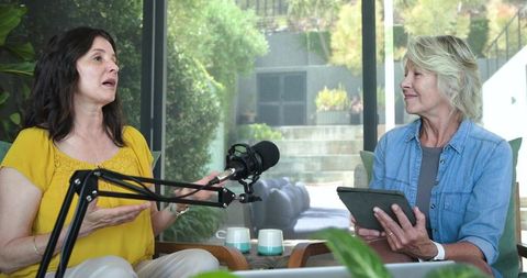 Women recording relaxed podcast interview in sunlit living room with tablet