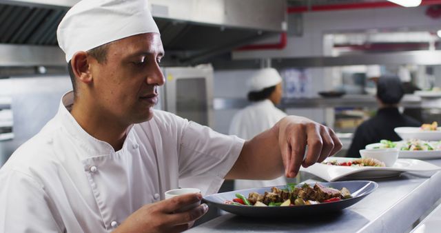Caucasian male chef garnishing dish and smiling in restaurant kitchen. Working in a busy restaurant kitchen.