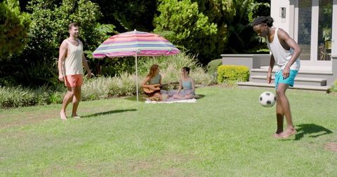 Diverse friends relaxing in sunny backyard with guitar playing