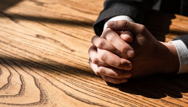 Clasping hands resting on wooden table conveying tension and focus