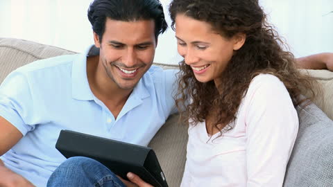 Couple Smiling While Using Tablet on Cozy Sofa