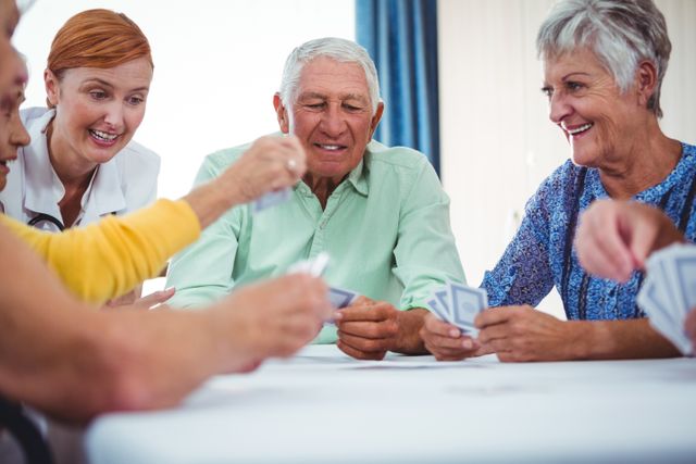 Smiling nurse and seniors people playing cards in a retirement home