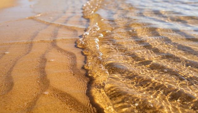 Golden shallow wave lapping sandy shoreline with shimmering caustics and rippled sand