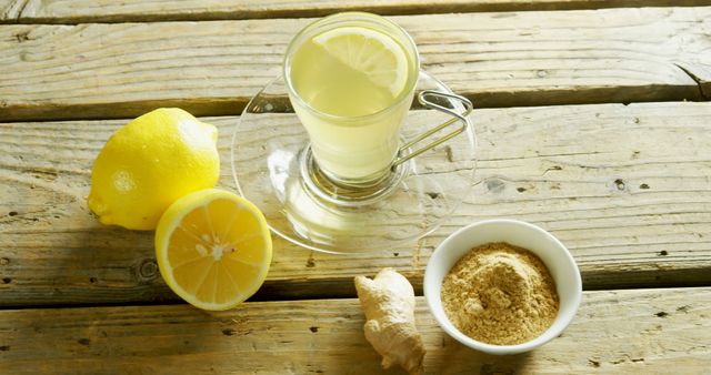 A glass of lemon ginger tea sits on a rustic wooden table, accompanied by fresh lemons and a bowl of ground ginger. Lemon ginger tea is popular for its health benefits, including aiding digestion and boosting immunity.