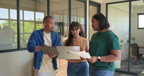 African american coworkers collaborating and reviewing documents with tablet in office