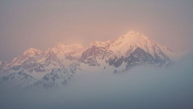 Pink Alpenglow on Snow-Covered Mountain Peaks with Mist