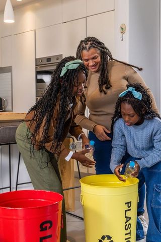African american mom and daughters sorting plastic bottles for recycling in modern kitchen