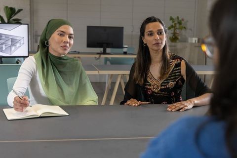 Muslim woman wearing hijab and colleague reviewing 3d floorplan, collaborating in modern office