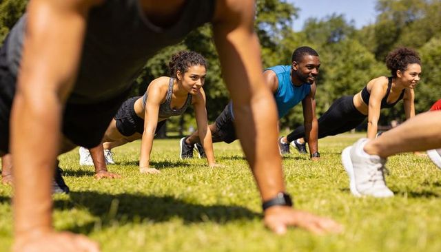 Group holding plank in park during outdoor fitness class — team training and core workout