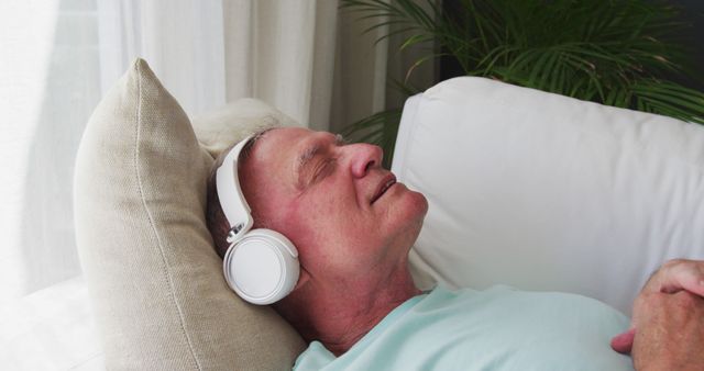 Caucasian senior man wearing headphones singing while lying on the couch at home. staying at home in self isolation in quarantine lockdown