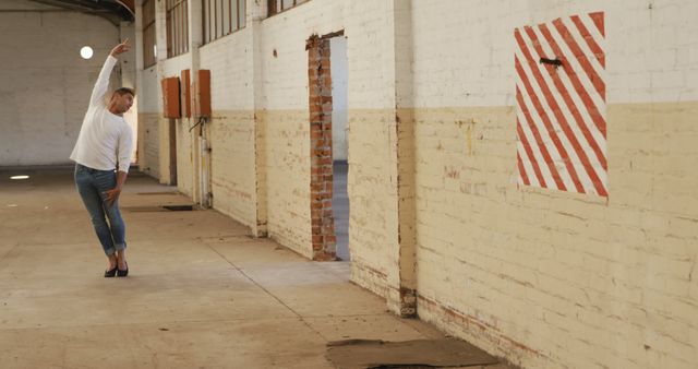 Man dancing alone in a large, empty industrial warehouse space with red striped wall in the background. Ideal for articles or visuals related to urban dance styles, modern art performance, industrial and urban architecture, creative expressions, and contemporary arts.