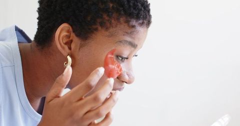 African american woman applying red hydrogel under-eye patch for skincare routine closeup