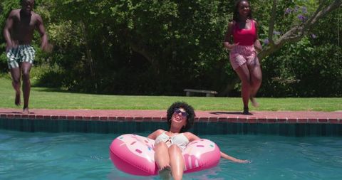 Friends relaxing on pink donut float in sunny backyard pool