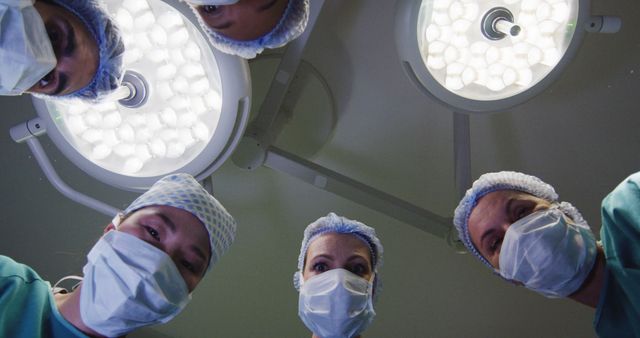 Image of patient view looking up at diverse group of surgeons and lights in operating theatre. Hospital, medical and healthcare services.