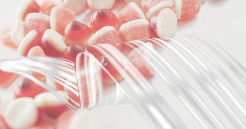 Glistening red-white gummy candy resting among clear curved strands with crystal sugar