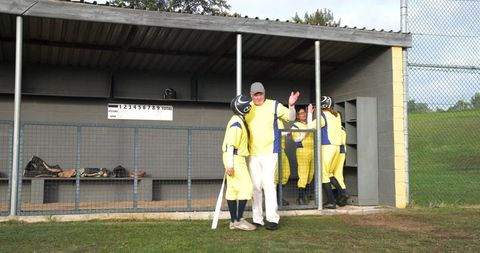Senior male coach supporting female softball player in dugout setting