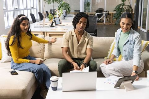 Diverse team collaborating in modern open-plan office reviewing charts on laptop and tablet