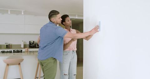 Couple Interacting with Smart Thermostat in Modern Kitchen