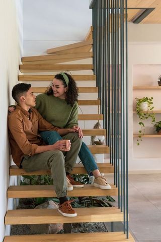 Young couple sitting on floating wooden stairs sharing coffee in modern minimalist home