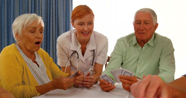 Senior citizens are engaging in a card game, accompanied by a nurse. This depicts a lively and interactive environment in a retirement or nursing home. Useful for portraying elderly care, group activities in senior communities, or lifestyle of senior citizens.